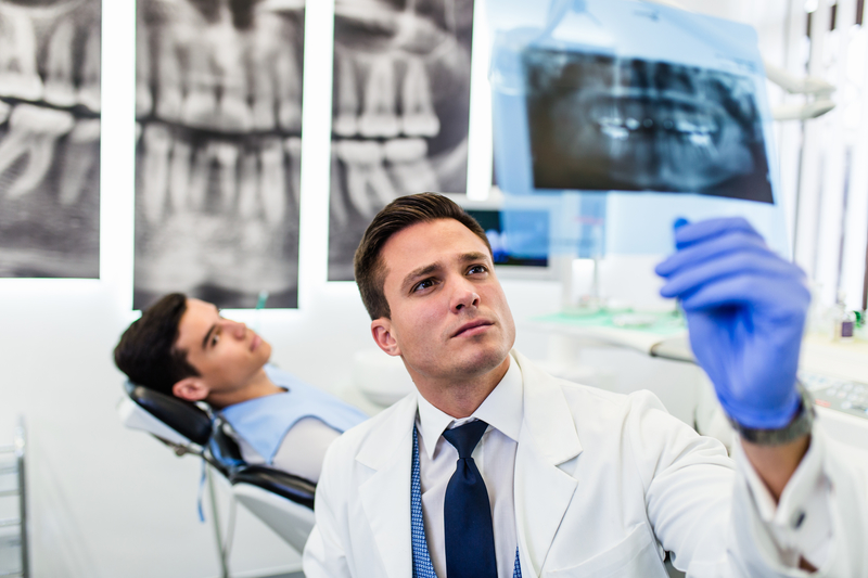 Photo of smiling male dentist looking at patient's x-ray of teeth