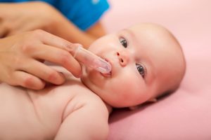 Mother cleaning baby's mouth with special fingertip brush for children