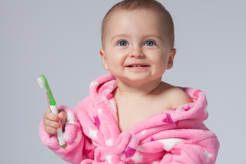 Baby in pink robe holding toothbrush in hand