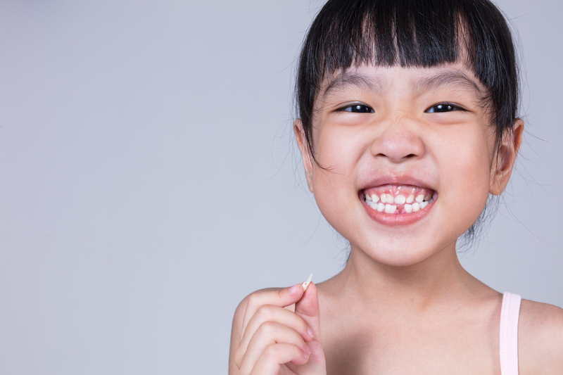 Young Asian girl holding her missing tooth while smiling