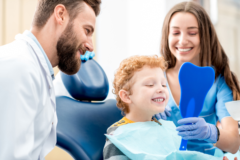 Child looking at teeth in mirror with dentist and assistant