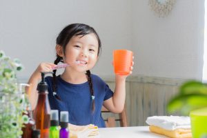 Young asian girl that is brushing her teeth and holding a glass of water. 