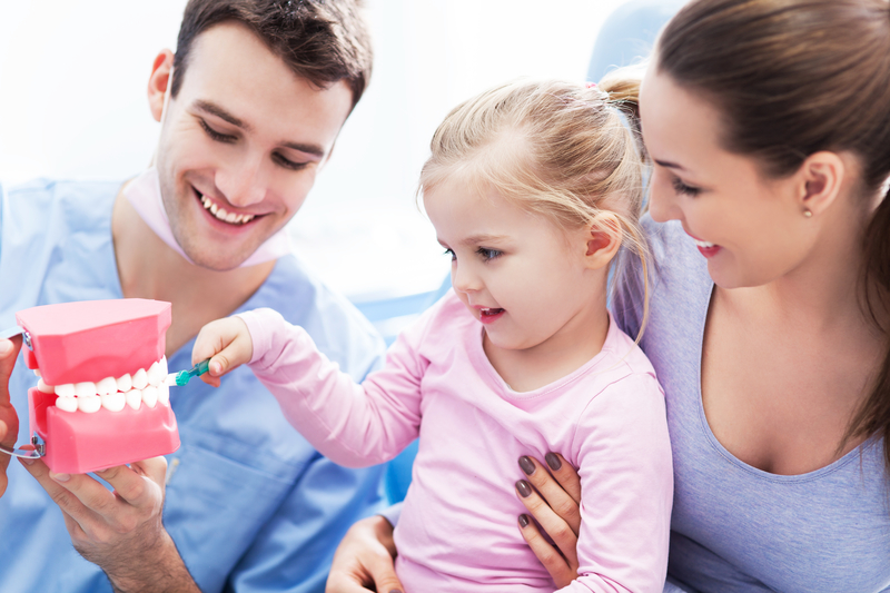A young man and a young woman holding a small girl and showing her how to brush teeth on a dental model