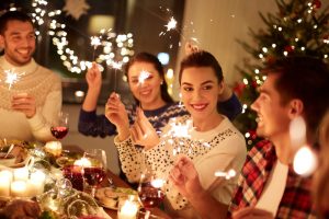 A table of friends that are celebrating the holidays. They are smiling and laughing and have sparklers in their hands. 