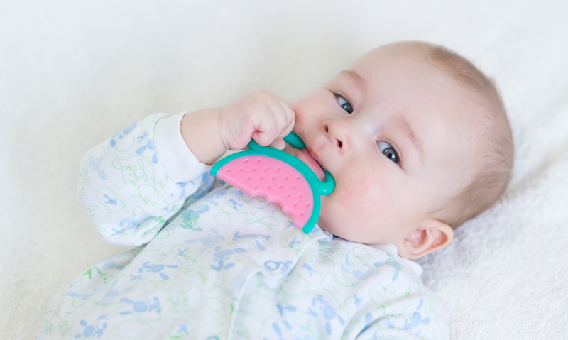A baby chewing on a teething ring toy.