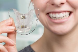 Young woman smiling while holding teeth retainer in hand