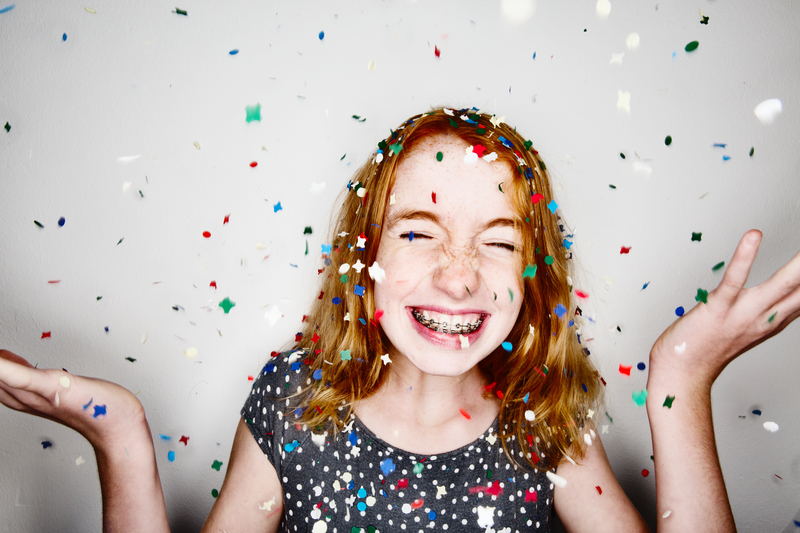 Redheaded teenager throwing confetti in the air while smiling with braces
