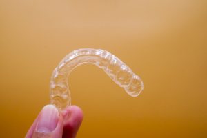 Person holding an Invisalign retainer on an orange background