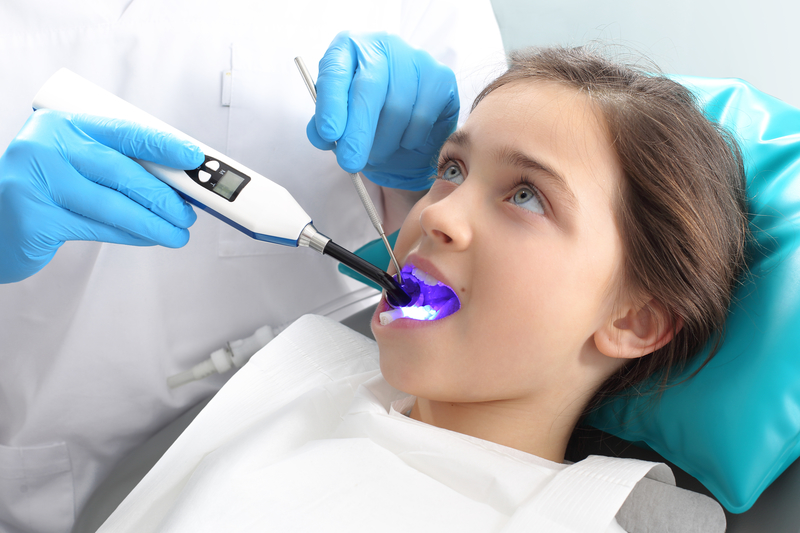 young female child sitting in dental chair getting laser treatment done by dentist