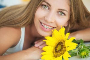 Young woman that has braces on her teeth. She is smiling at the camera with a sunflower in front of her.