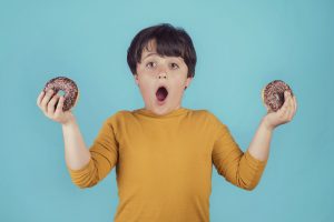 Image of a boy holding donuts in his hands with a surprised look on his face.